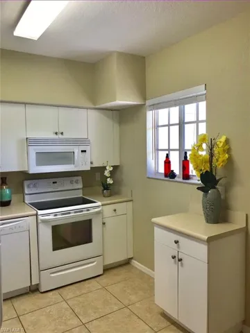 Kitchen with white appliances, white cabinets, light countertops, light tile patterned flooring, and a textured ceiling
