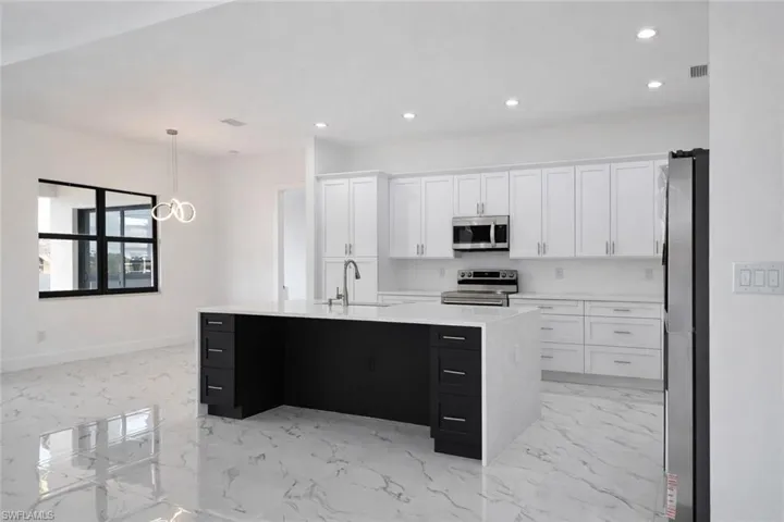 Dual tone kitchen with stainless steel appliances, light stone counters, a kitchen island with sink, hanging light fixtures, and light marble finish flooring