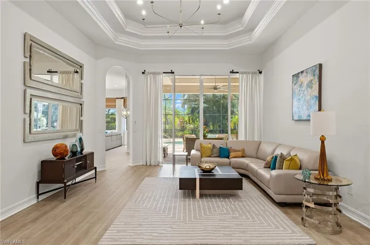 Living room with a tray ceiling, ornamental molding, light wood-type flooring, and a healthy amount of sunlight