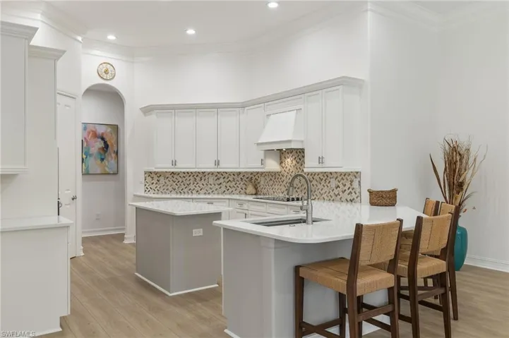 Kitchen featuring light hardwood / wood-style flooring, custom range hood, kitchen peninsula, a breakfast bar, and white cabinets