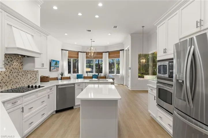 Kitchen with kitchen peninsula, appliances with stainless steel finishes, light wood-type flooring, crown molding, and decorative light fixtures