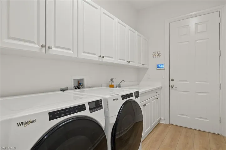 Laundry area with light hardwood / wood-style floors, washing machine and dryer, sink, and cabinets