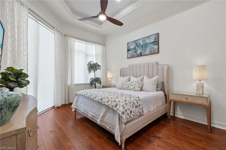 Bedroom with ornamental molding, a tray ceiling, dark wood-type flooring, and ceiling fan