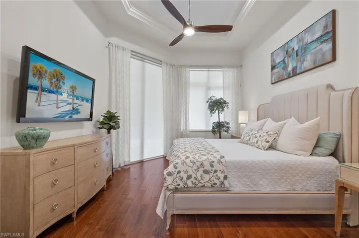Bedroom featuring dark wood-type flooring, ceiling fan, a raised ceiling, and ornamental molding