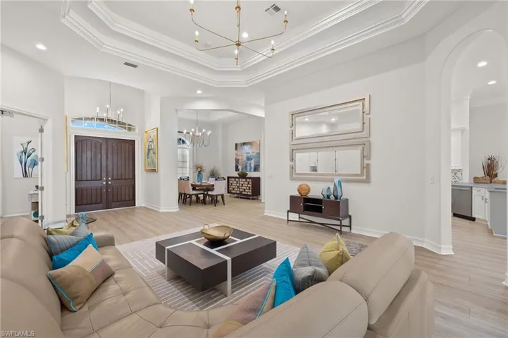 Living room featuring a towering ceiling, light hardwood / wood-style flooring, ornamental molding, and a tray ceiling