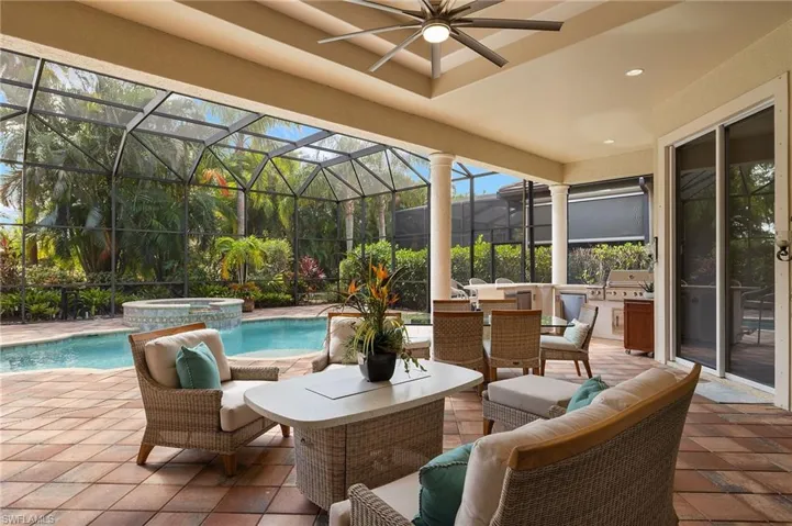 View of patio with glass enclosure, a pool with hot tub, grilling area, ceiling fan, and pool water feature