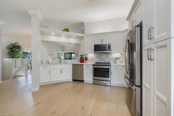 Kitchen featuring white cabinetry, stainless steel appliances, backsplash, ornamental molding, and light wood-style flooring