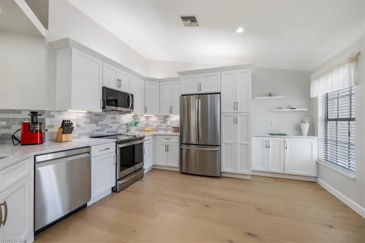 Kitchen featuring stainless steel appliances, white cabinetry, light wood finished floors, crown molding, and recessed lighting