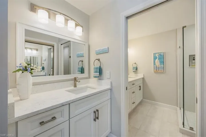 Full bath featuring two vanities, light tile patterned flooring, and a shower stall