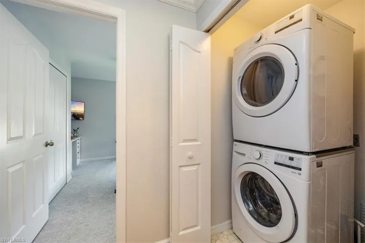 Laundry area featuring stacked washing machine and dryer and light colored carpet