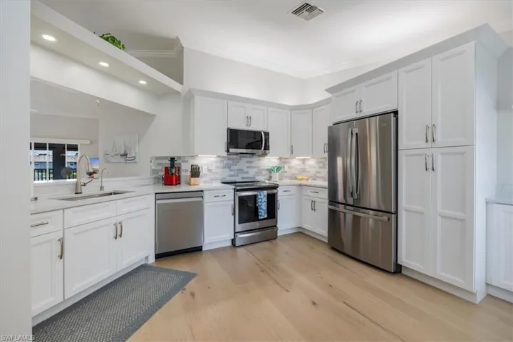 Kitchen with stainless steel appliances, white cabinetry, backsplash, light wood-style flooring, and crown molding