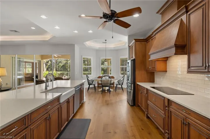 Kitchen with decorative light fixtures, custom exhaust hood, stainless steel appliances, a raised ceiling, and light hardwood / wood-style flooring