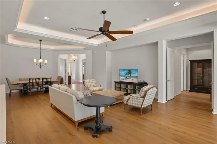 Living room featuring ceiling fan with notable chandelier, light hardwood / wood-style floors, and a raised ceiling