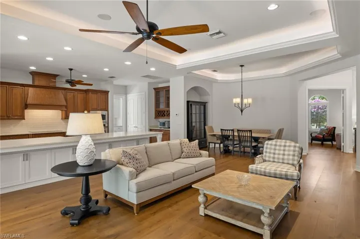 Living room with ceiling fan with notable chandelier, light hardwood / wood-style floors, and a raised ceiling