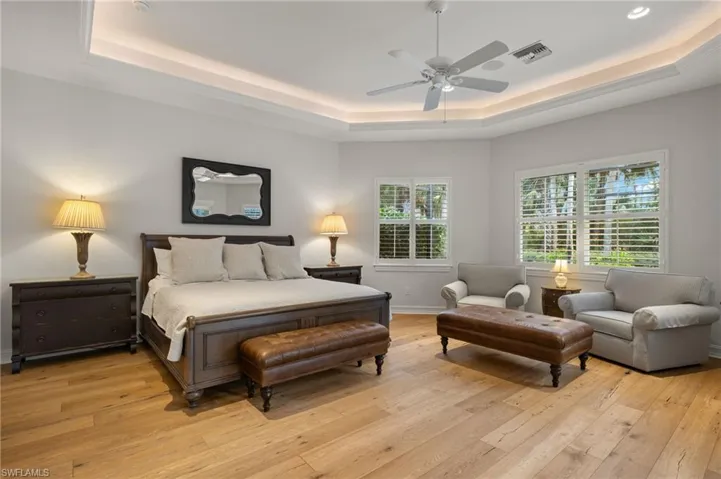 Bedroom with ceiling fan, light hardwood / wood-style floors, and a tray ceiling