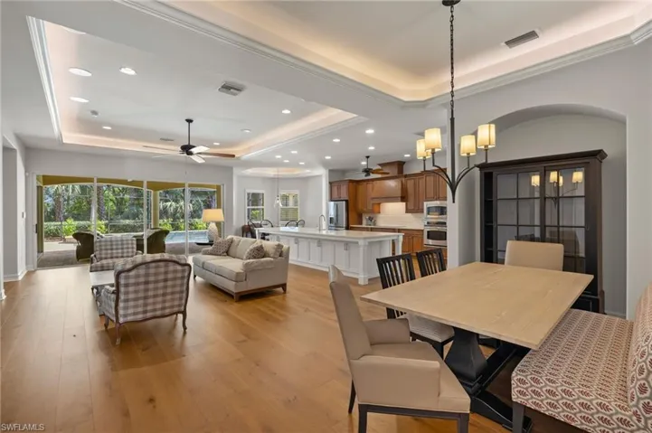 Dining room featuring ceiling fan with notable chandelier, light hardwood / wood-style flooring, and a raised ceiling