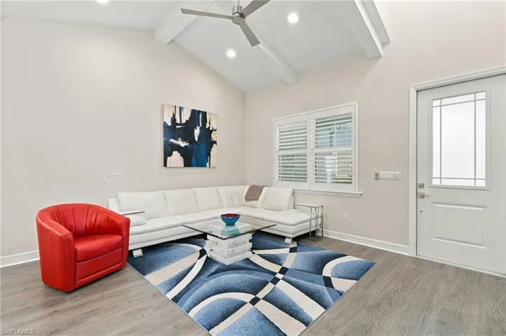 Vaulted ceiling with exposed beams, wood-finish flooring, plantation shutters, recessed lighting, and a modern ceiling fan