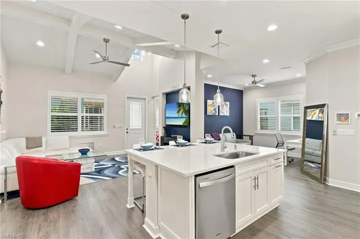 Open-concept living space with exposed beam ceiling, recessed lighting, wood-finish flooring, a kitchen island with integrated sink, and white cabinetry