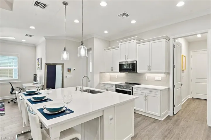Kitchen featuring white shaker cabinetry, stainless steel appliances, a subway tile backsplash, and a large island with an undermount sink