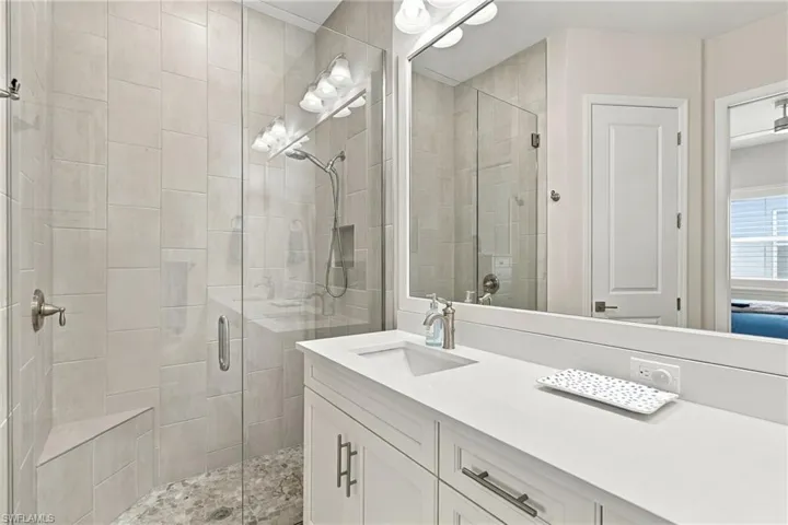 Glass-enclosed shower with a built-in bench, pebble-tile flooring, and a wall-mounted shower head