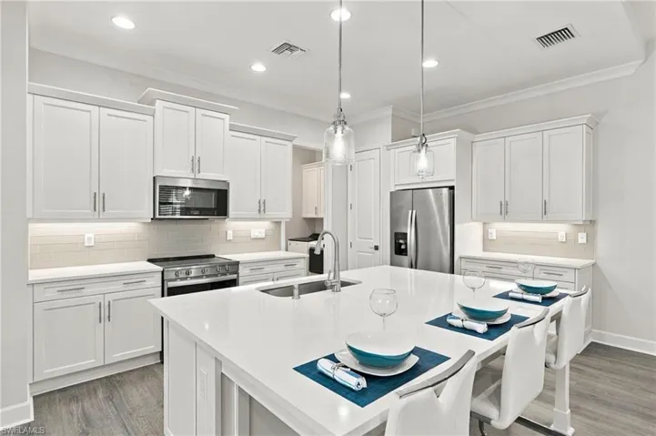 Kitchen featuring white cabinetry, stainless steel appliances, a large center island with integrated sink, pendant lighting, and wood-finish flooring