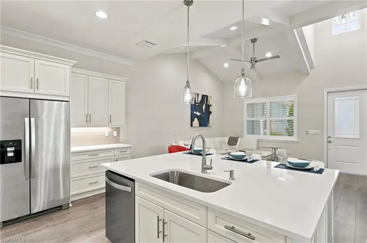 Kitchen featuring a large island with an undermount sink, stainless steel appliances, white cabinetry, wood-finish flooring, and a vaulted ceiling with exposed beams