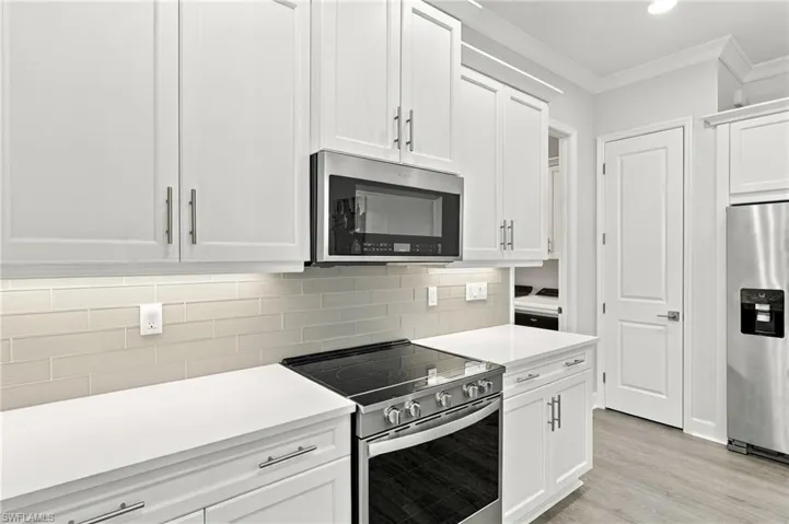 White shaker cabinetry with brushed nickel hardware, stainless steel appliances, light-toned subway tile backsplash, white countertops, and wood-finish flooring