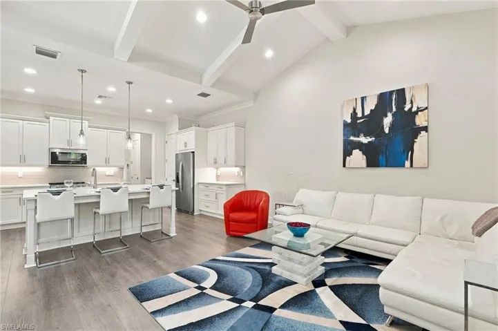 Vaulted ceiling with exposed beams, wood-finish flooring, white cabinetry, stainless steel appliances, and a kitchen island with pendant lighting