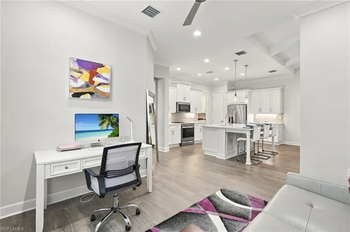 Open-concept living space featuring wood-finish flooring, a contemporary kitchen with stainless steel appliances, white cabinetry, a kitchen island with seating, and recessed lighting