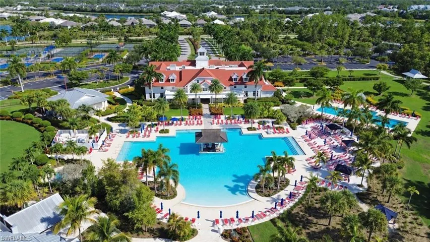 Expansive resort-style pool area with multiple swimming pools, a central building with red tile roofing, surrounding green spaces, and tennis courts