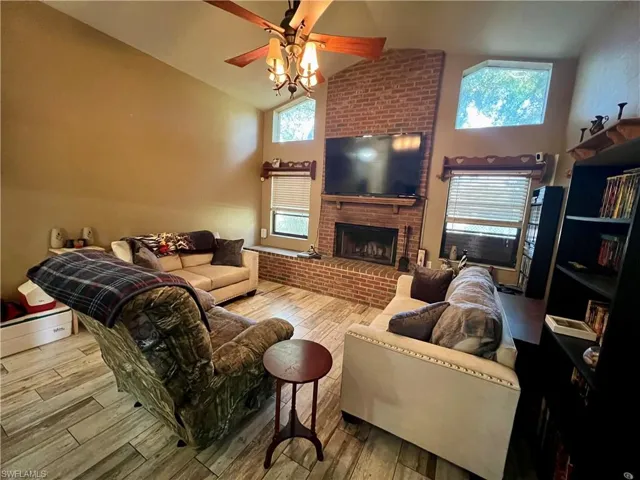 Living room with a fireplace, light wood plank tile flooring, vaulted ceiling, and ceiling fan