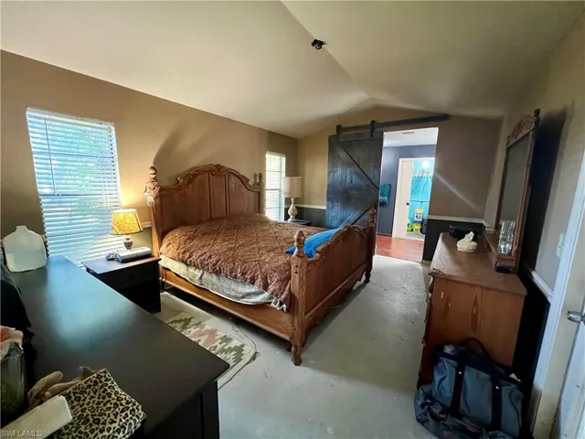 Primary Bedroom with a barn door, multiple windows, and lofted ceiling