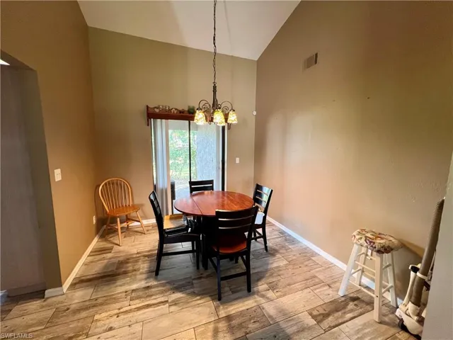 Dining area featuring high vaulted ceiling, light wood plank tile floors.