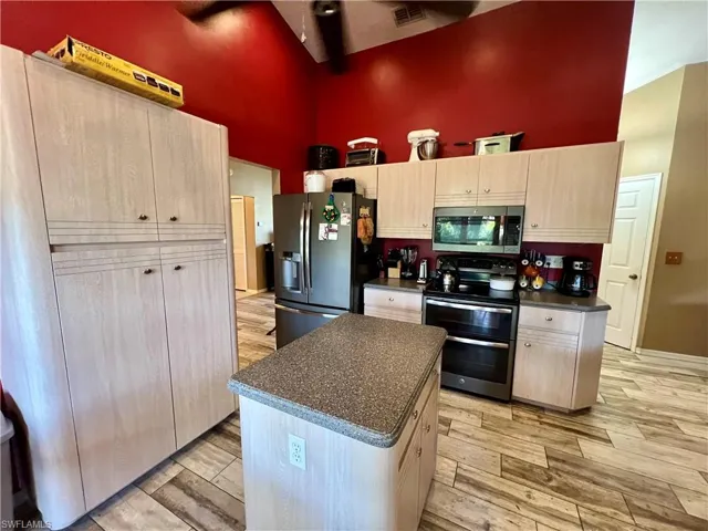Kitchen with a high ceiling, a kitchen island, light wood-plank tile flooring, and appliances with stainless steel finishes