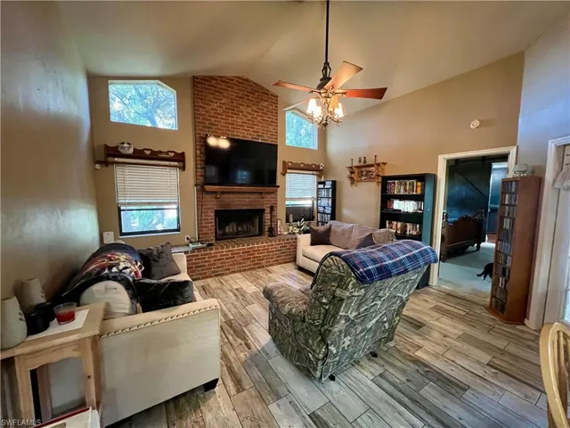 Living room with a fireplace, wood plank tile floors,  ceiling fan, and high vaulted ceiling