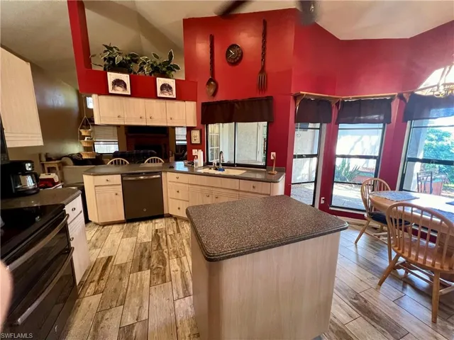 Kitchen featuring high vaulted ceiling, stainless steel dishwasher, black stove, and wood plank tile floors