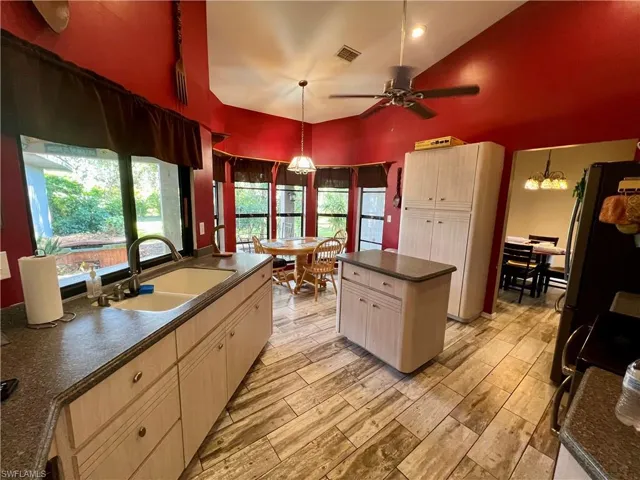 Kitchen featuring a center island, light colored wood plank tile floors, hanging light fixtures, sink, and ceiling fan with notable chandelier