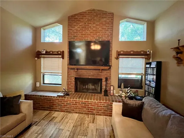 Family room with light wood plank tile flooring, vaulted ceiling, a healthy amount of sunlight, and a brick fireplace