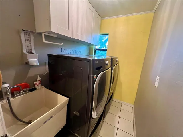 Laundry area featuring cabinets, sink, light tile patterned floors, washer and clothes dryer.