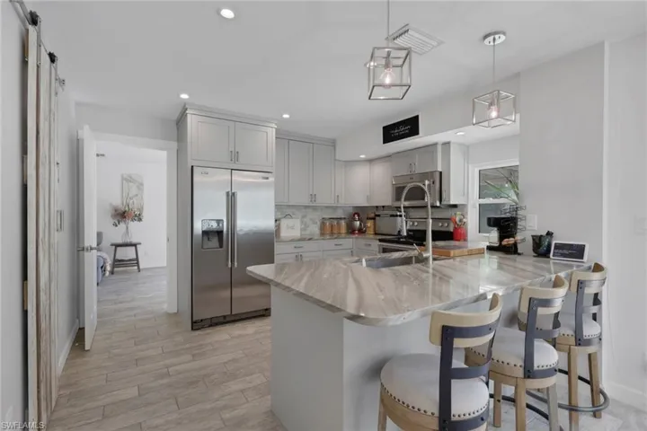 Beautifully updated kitchen with Quartz countertops, Gray wood shaker cabinets, glass backsplash, newer appliances, deep kitchen sink, seating area, perfect view of the pool/patio area, and a large walk in pantry with barn door.