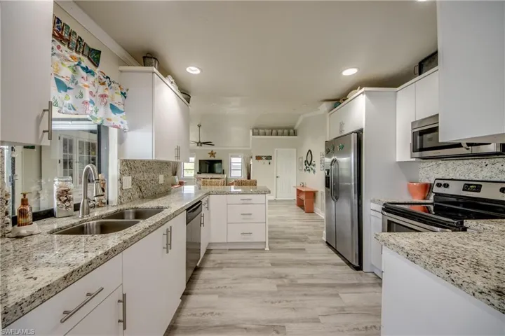 Kitchen featuring a peninsula, a sink, light stone counters, and appliances with stainless steel finishes