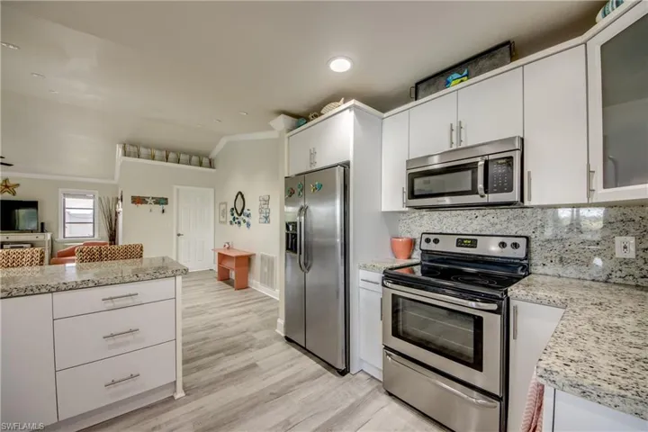 Kitchen with crown molding, backsplash, white cabinetry, and stainless steel appliances