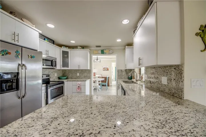 Kitchen with glass insert cabinets, a sink, appliances with stainless steel finishes, white cabinetry, and light stone counters