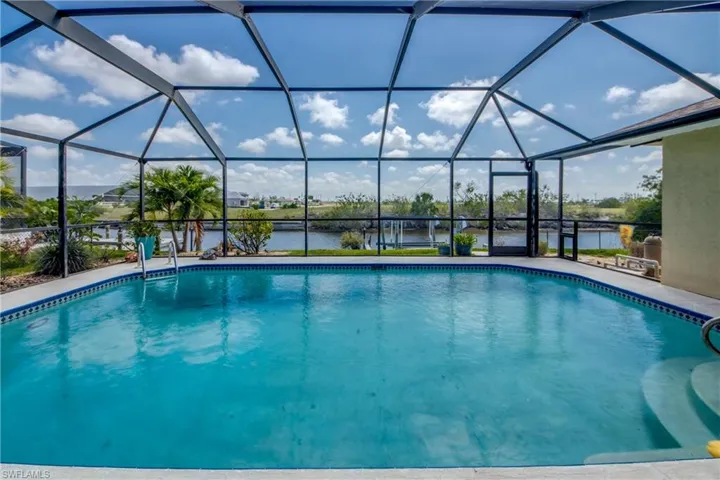 Outdoor pool with a water view, a patio area, and glass enclosure