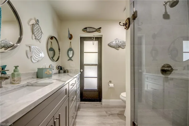 Bathroom with double vanity, toilet, a shower stall, a sink, and wood finished floors