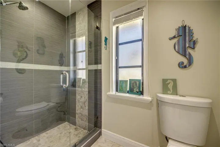 Bathroom featuring toilet, marble finish floor, a stall shower, and baseboards