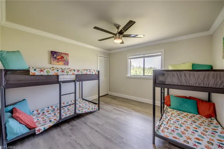 Bedroom with a closet, baseboards, crown molding, a ceiling fan, and wood finished floors
