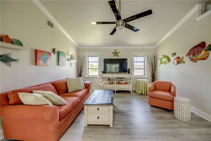 Living area featuring visible vents, baseboards, ornamental molding, ceiling fan, and wood finished floors