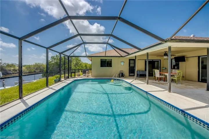 Outdoor pool featuring a patio, a ceiling fan, a water view, and glass enclosure