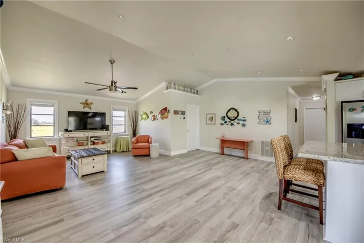 Living area with ornamental molding, visible vents, light wood-type flooring, and vaulted ceiling